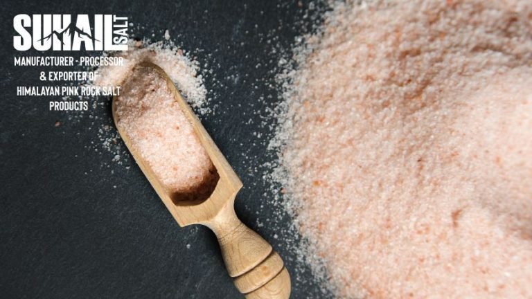 A wooden board showcasing a contrast of Himalayan Pink Salt crystals in a ceramic grinder next to a bowl of fine, off-white Sea Salt, with a lemon wedge and rosemary sprig.